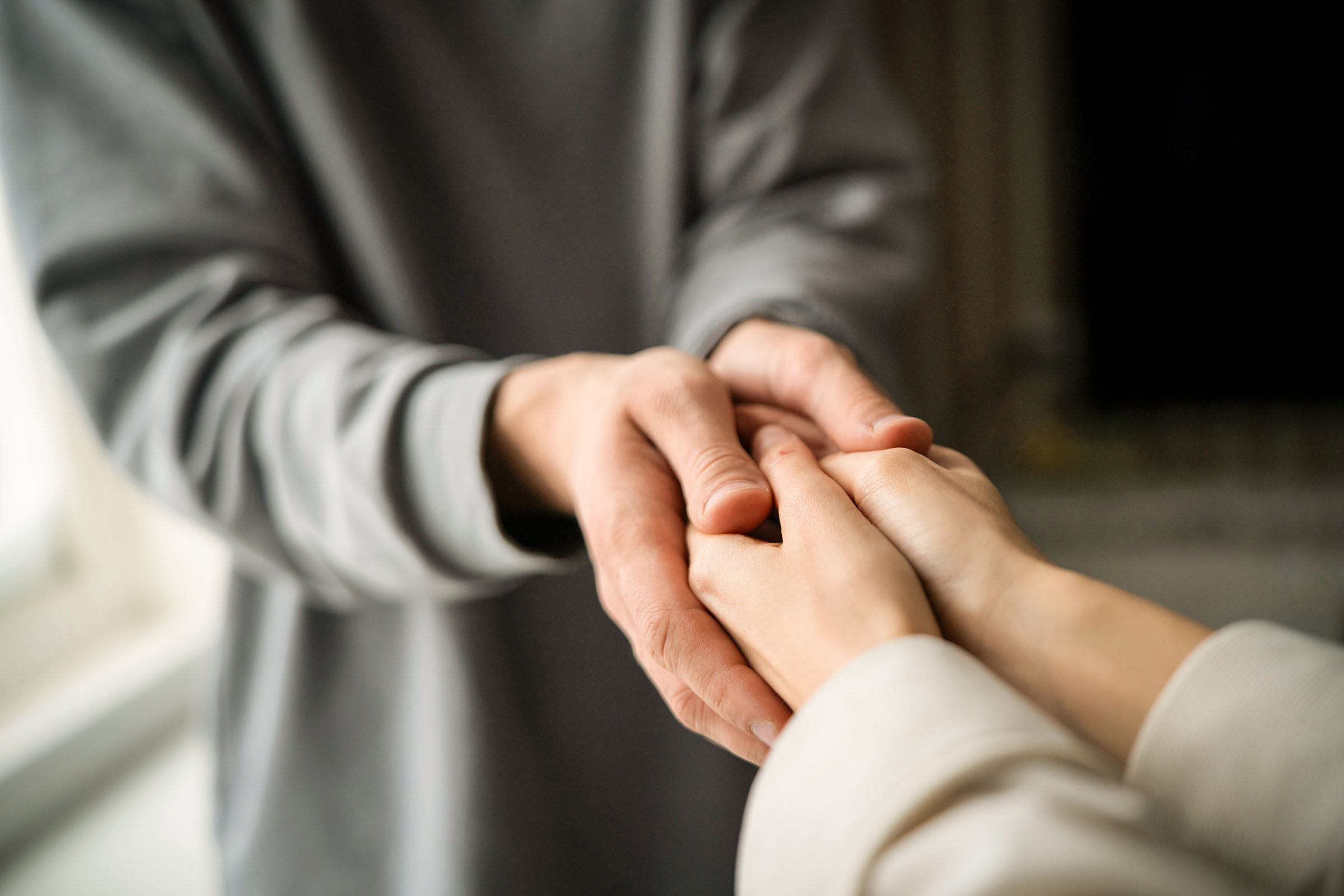 Two people engage in a compassionate touch, offering emotional support through a simple but powerful gesture of connected hands.